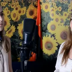 Dwie kobiety, być może żona Miłosza Motyki, stoją przed mikrofonem na tle słoneczników.