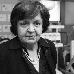 Portret starszej kobiety, Margaret Religa, w czarnej bluzce i naszyjniku z pereł, na tle ścian z logo.