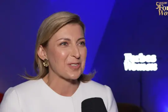 Olga Leonowicz w białej marynarce, podczas wywiadu na tle neonu Forbes Women.