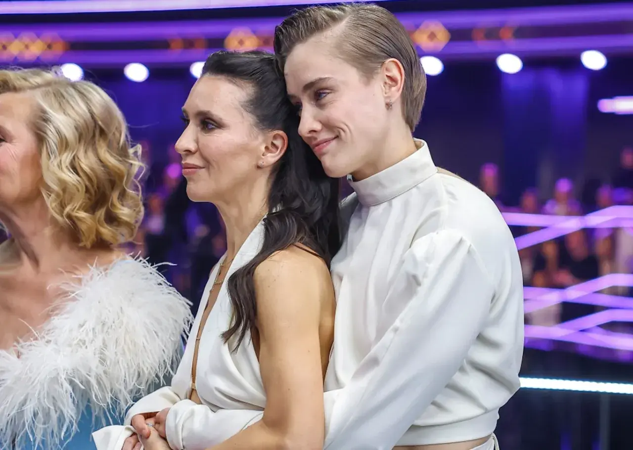 Katarzyna Zillmann i jej partnerka w białych strojach, czule objęte, na tle fioletowych świateł.