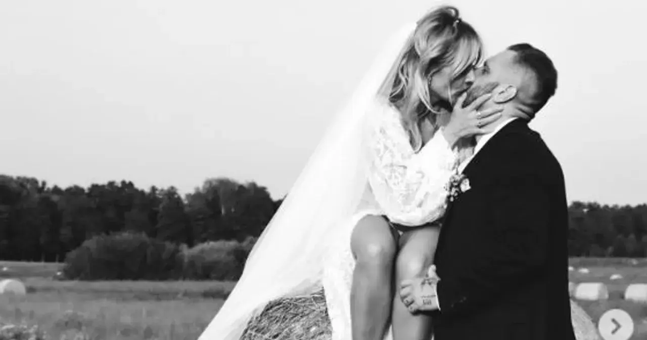 Patrycja Markowska i jej mąż w czułym uścisku na tle wiejskiego krajobrazu.