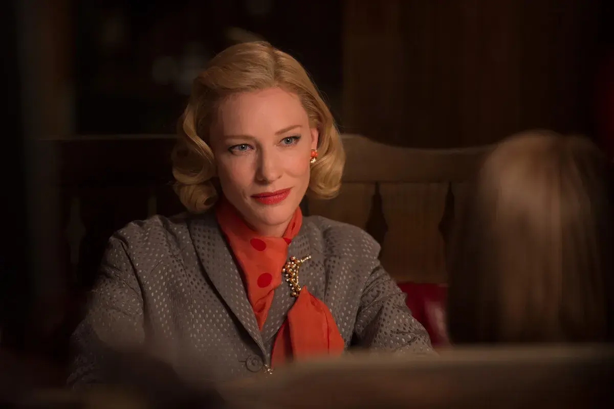 Cate Blanchett w eleganckiej stylizacji, z rudym szalem i broszką, w scenie z jednego ze swoich filmów.