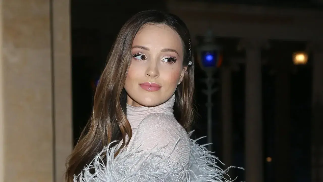 Elegancka żona Szczęsnego w błyszczącej sukni z piórami, z delikatnym makijażem i perłową spinką we włosach.