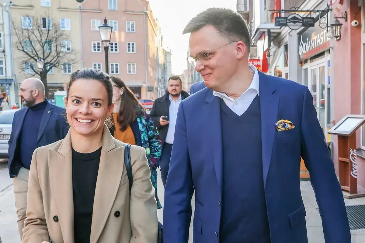 Aleksandra z mężem, Leo, spacerują ulicą. Uśmiechnięta para w eleganckich strojach.