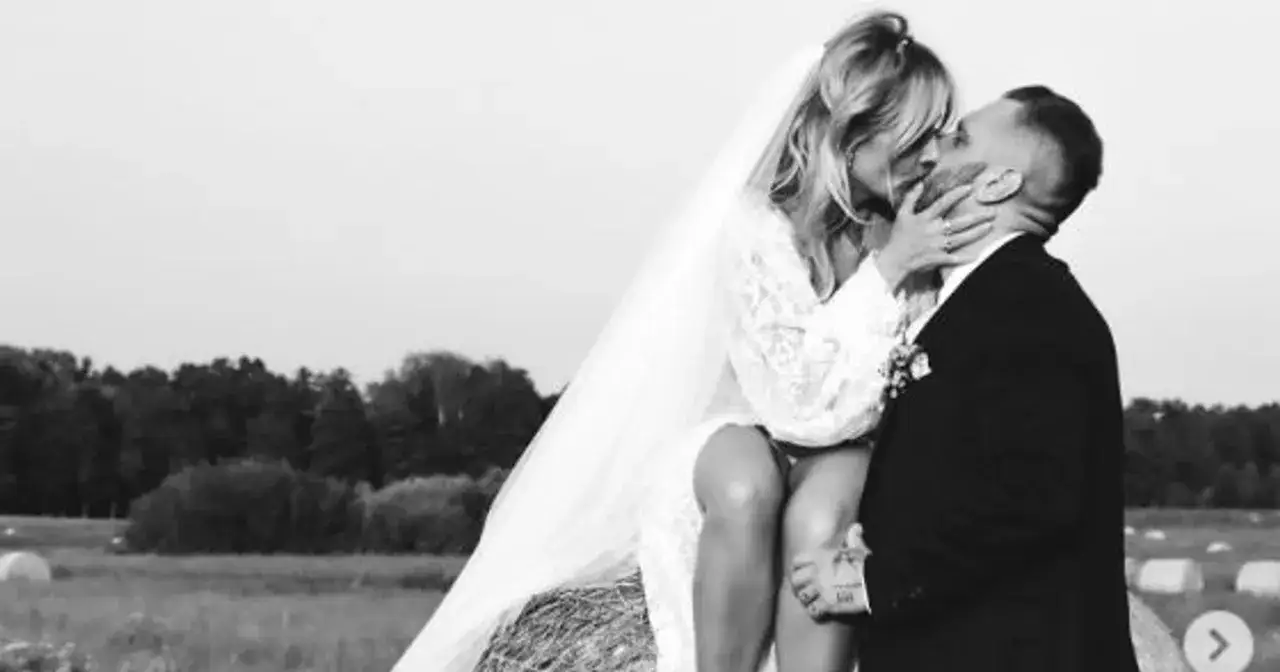 Patrycja Markowska i jej mąż w czułym uścisku na tle wiejskiego krajobrazu.