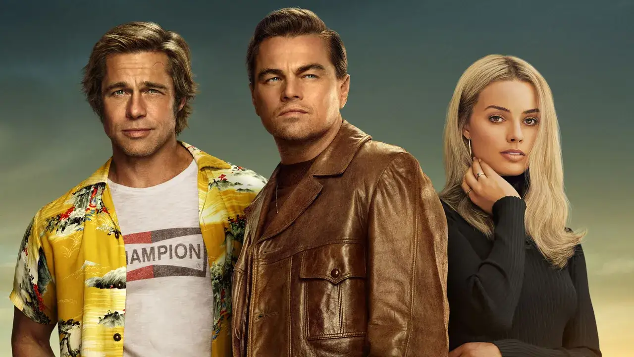 Brad Pitt, Leonardo DiCaprio i Margot Robbie w kadrze z filmu. Brad Pitt w żółtej koszuli i białej koszulce z napisem 