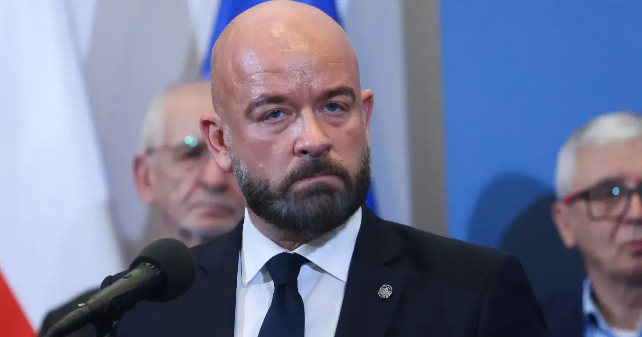 Jacek Sutryk z partnerem, w garniturze i z brodą, przemawia do mikrofonu.