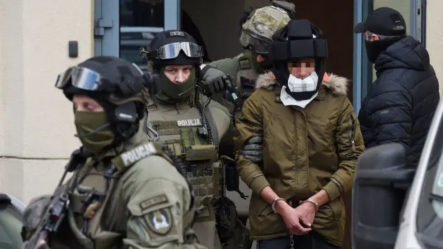 Kajetan Poznański w kajdankach, eskortowany przez policję w pełnym rynsztunku.